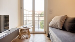 A modern living room with a sofa, a small round table with a book, and a large sliding glass door leading to a balcony. - Easylife - Style and balcony near the Duomo (Milano)