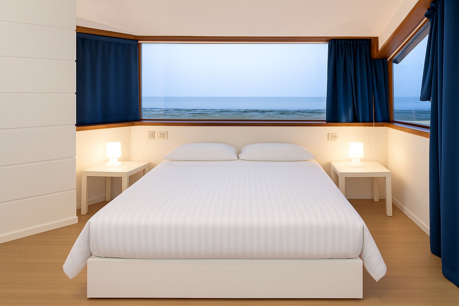 A bedroom with a large bed, two bedside tables with lamps, a view of the sea through a window, and blue curtains.