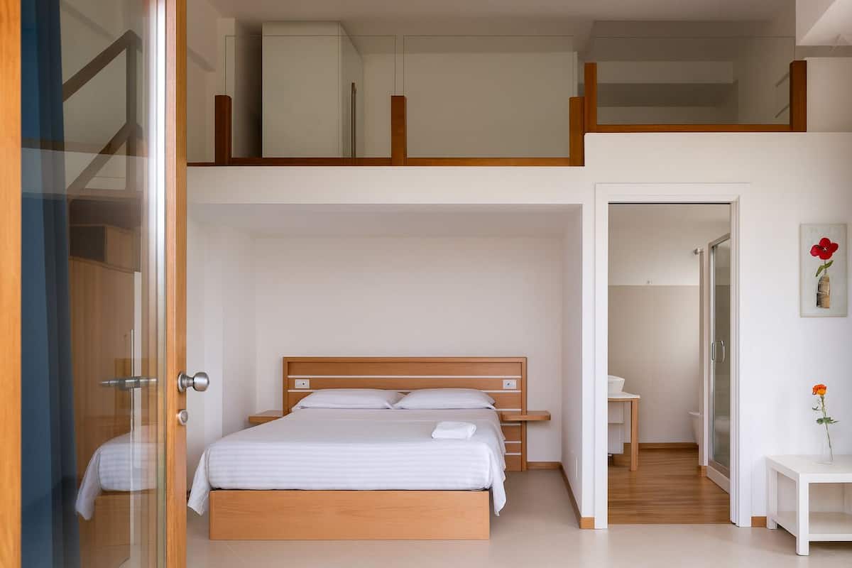 A modern bedroom with a loft-style bed, a small bedside table, and a walk-in closet.