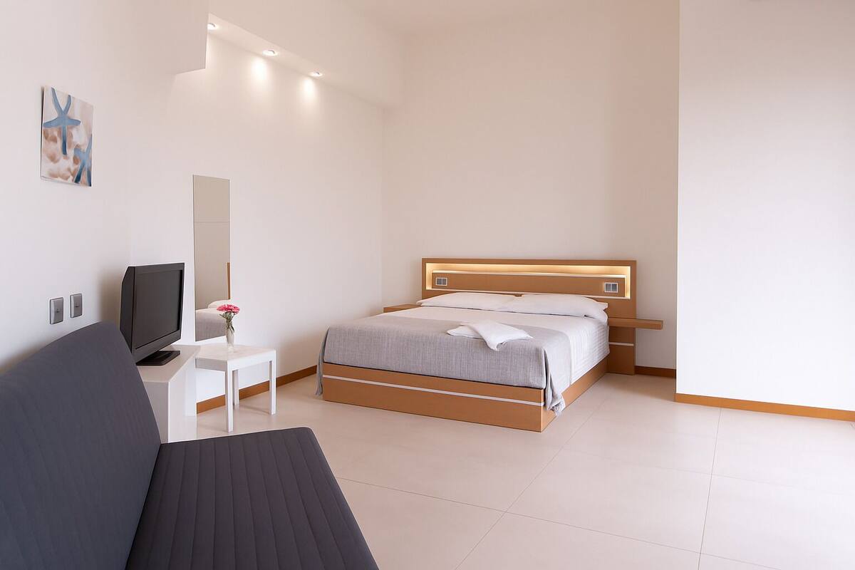 A modern hotel room with a bed, bedside table, TV, and a painting on the wall.