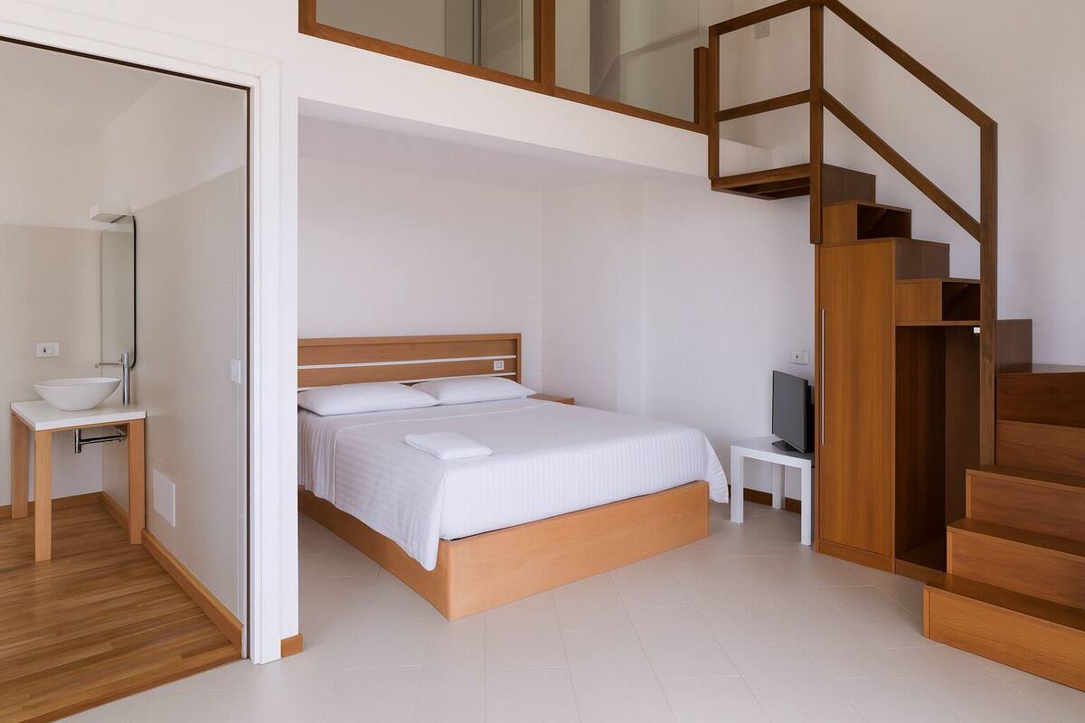 A modern bedroom with a wooden bed, a small bedside table with a TV, and a wooden staircase.