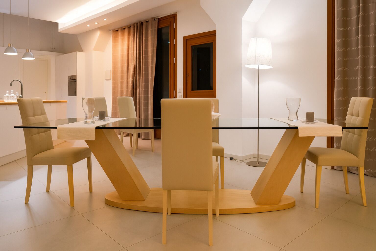 A modern dining area with a glass table and beige chairs, a kitchen in the background, and a floor lamp.