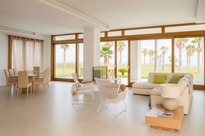 A spacious living room with a dining area, large windows with a view of palm trees, and a comfortable seating arrangement. - Lalena's Garden (Portopalo di Capo Passero)