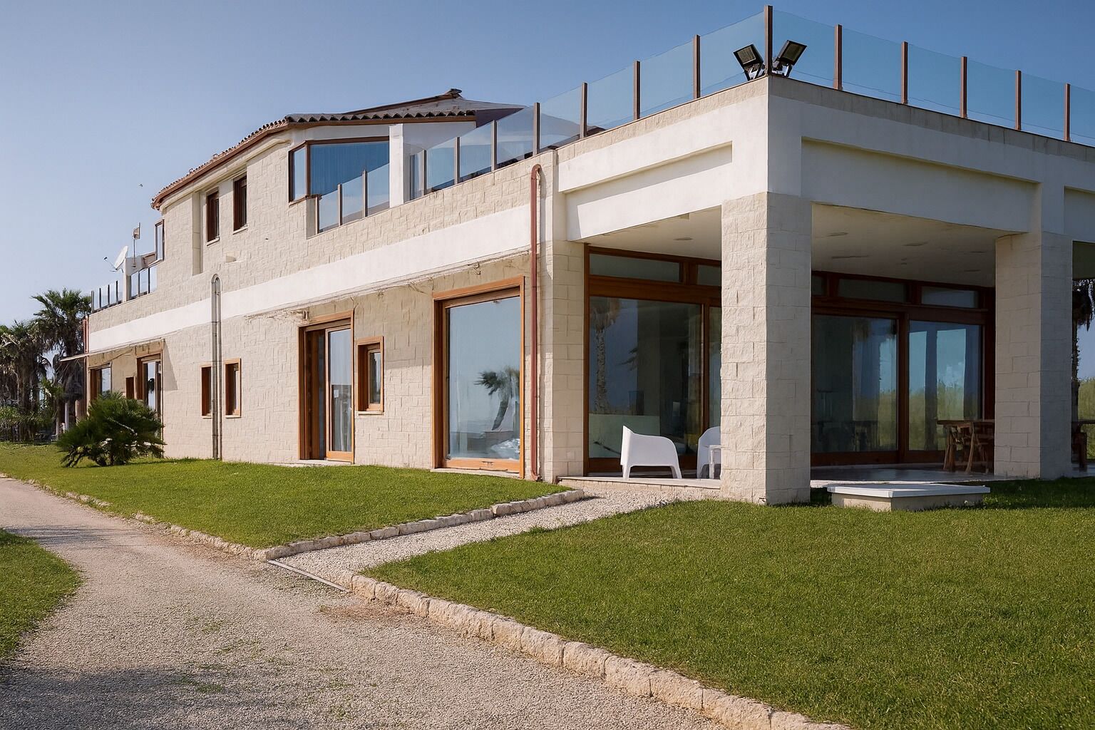 Ein modernes, zweistöckiges Haus mit großen Glasfenstern, einer überdachten Terrasse und einem gepflegten Rasen.