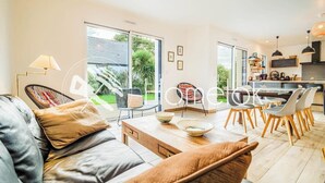 Ein modernes Wohnzimmer mit Sofa, Couchtisch und Essbereich mit Stühlen. Im Hintergrund ist eine Küche zu sehen.