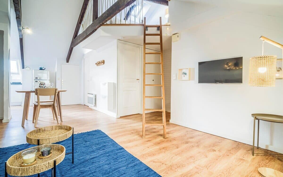 Een ruime kamer met een houten trap, een blauw vloerkleed en een televisie aan de muur.