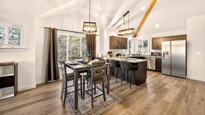 Een moderne keuken met een centraal eiland, roestvrijstalen apparatuur en een eethoek met vloerkleed en stoelen.