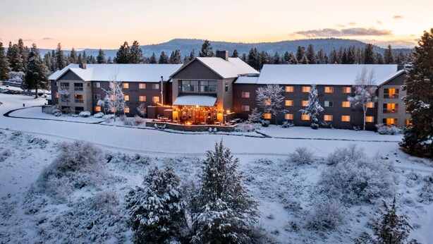 Een groot, meerhoog hotel met een centrale binnenplaats, omringd door met sneeuw bedekte bomen en een bergachtige achtergrond.