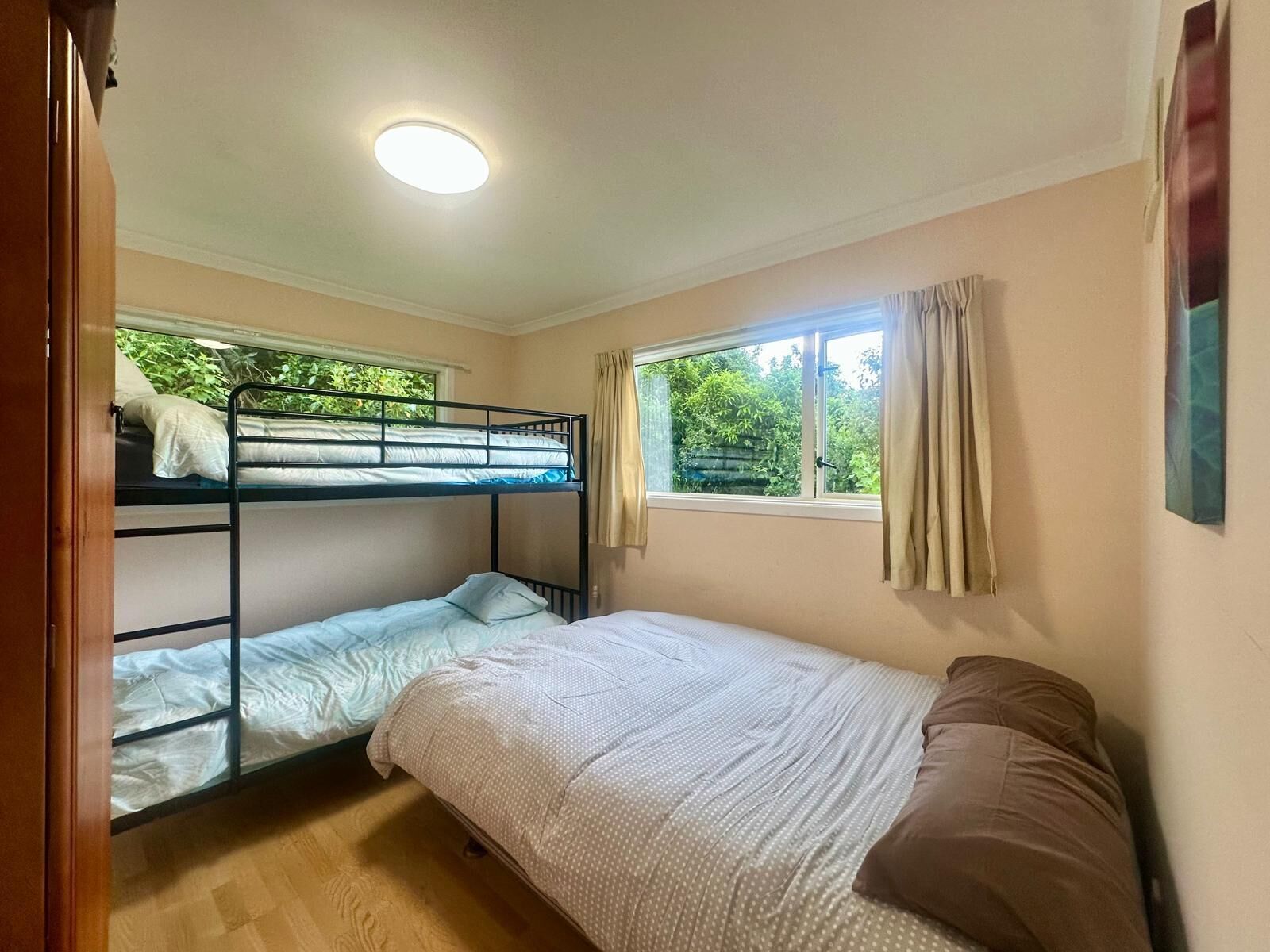 Et værelse med køjesenge, en enkelt seng, et vindue med gardiner og en loftlampe.