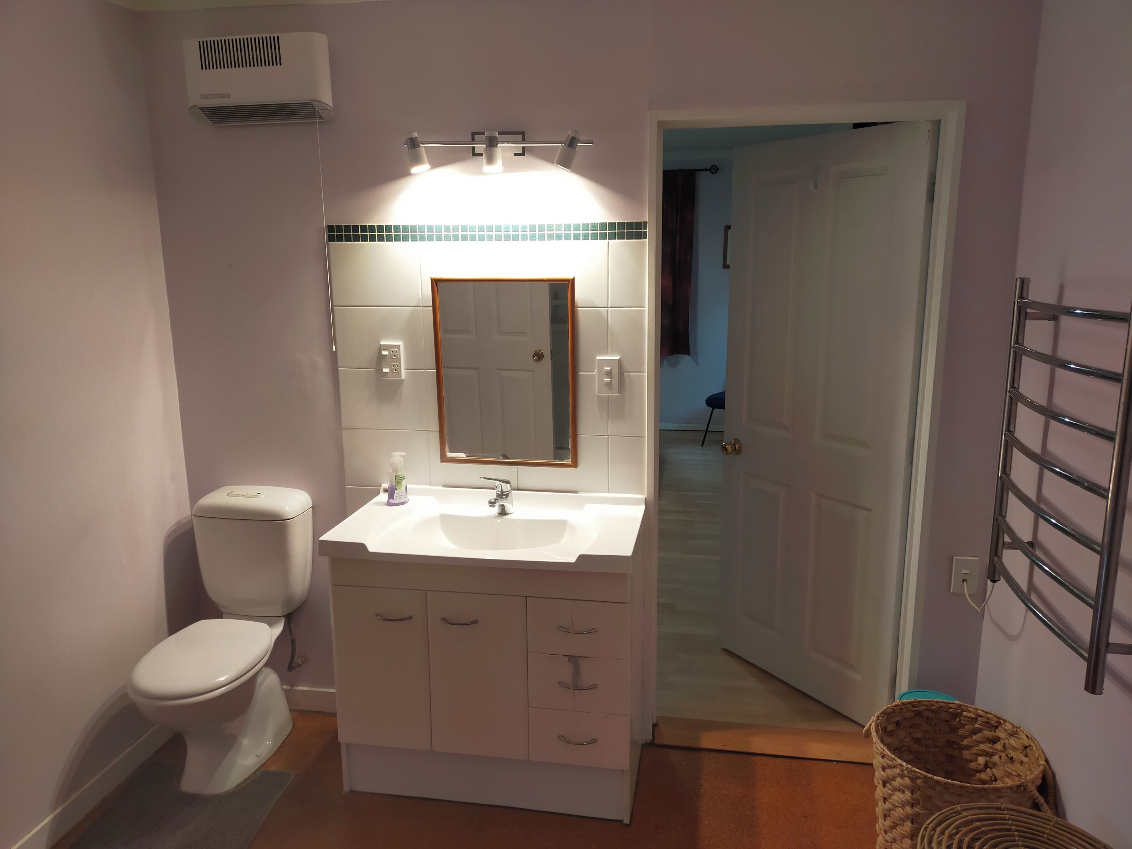 A bathroom with a toilet, sink, mirror, and a towel rack.