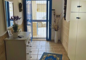 Ein Flur mit einem weißen Schrank, einem spiegel mit blauer Rahmung, einer Vase mit getrockneten Pflanzen und einem gemusterten Teppich.