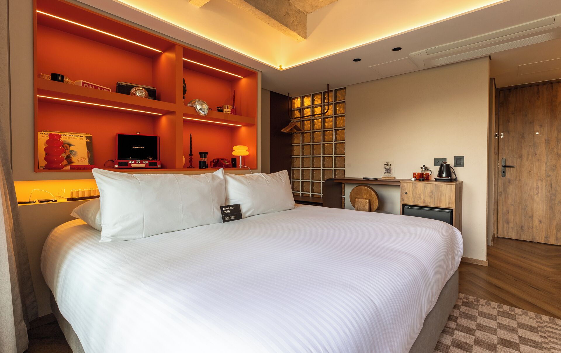 Una habitación de hotel con una cama grande, televisión, cafetera y estantería.