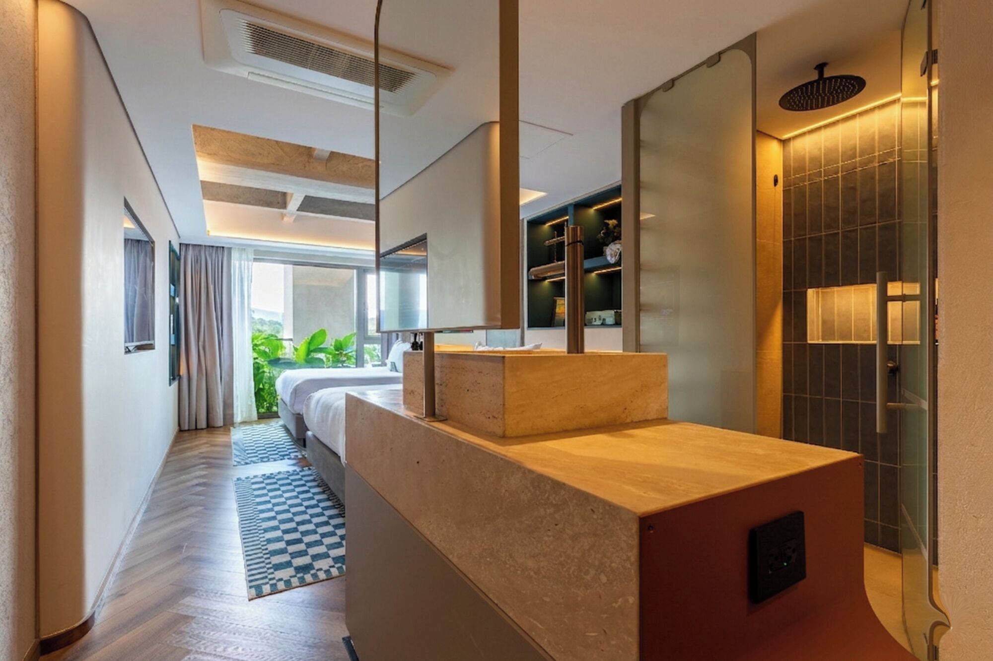 A modern hotel bathroom with a shower, a vanity with a mirror, and a view of greenery outside.