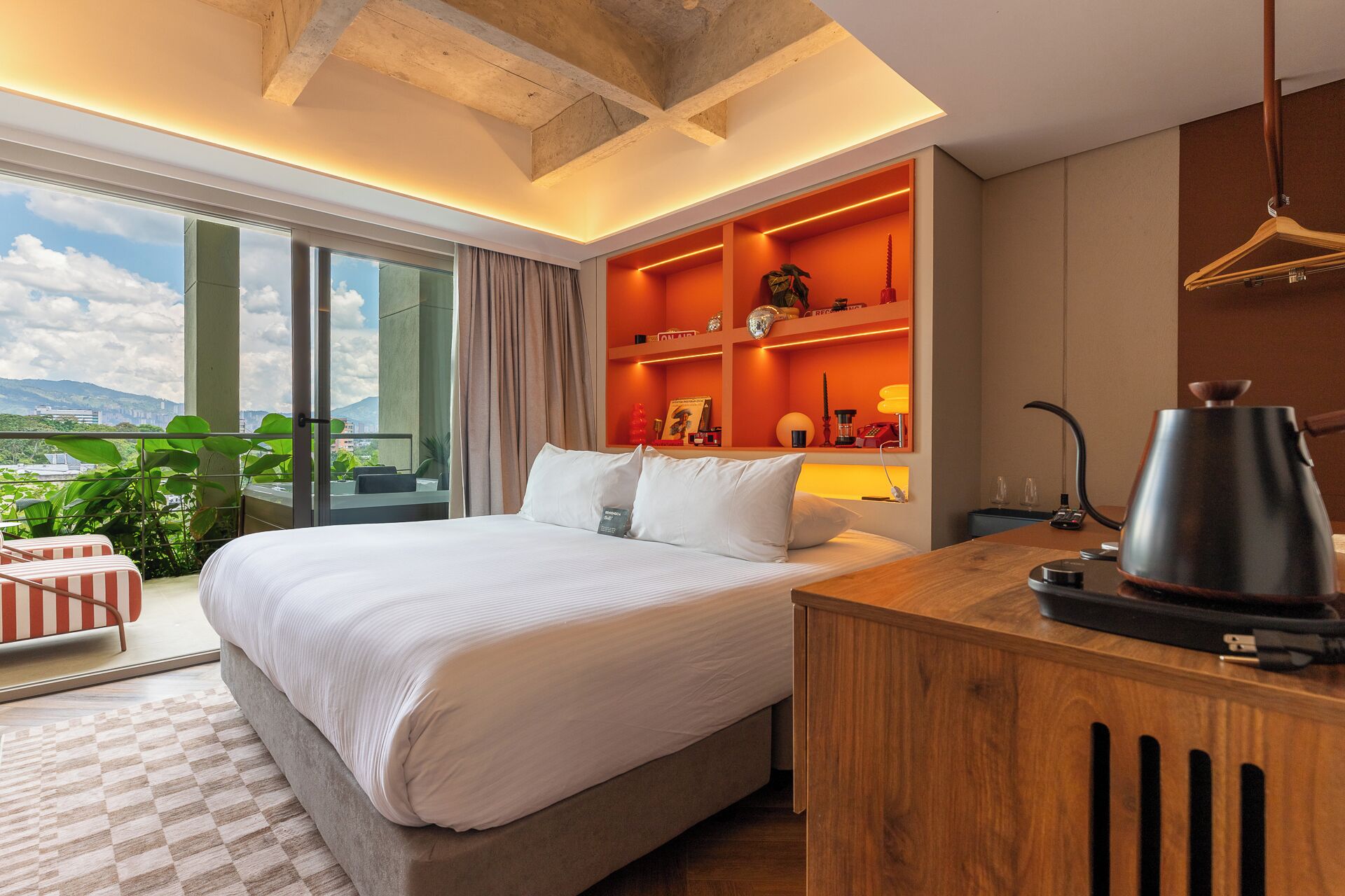 Quarto de hotel moderno com uma cama grande, uma escrivaninha de madeira, cafeteira e vista para a cidade.