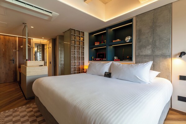 A modern hotel room with a large bed, built-in shelving with decorative items, a vanity with a mirror, and a checkered floor. - BoH Collection (Medellín)