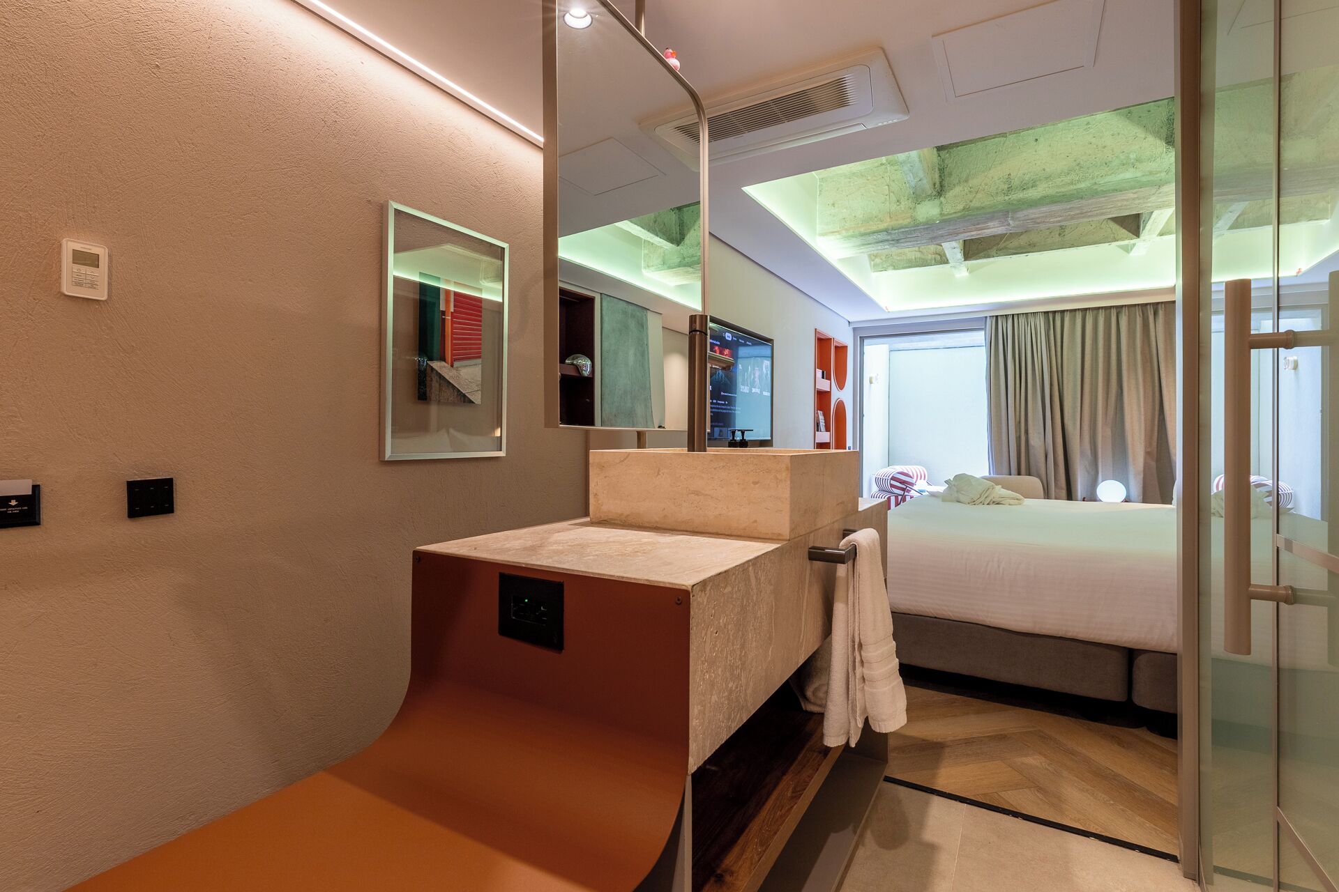 Ein modernes Hotelzimmer mit einem großen Bett, einem Badezimmer mit Waschbecken und Spiegel sowie einer Glastür, die auf einen Balkon führt.