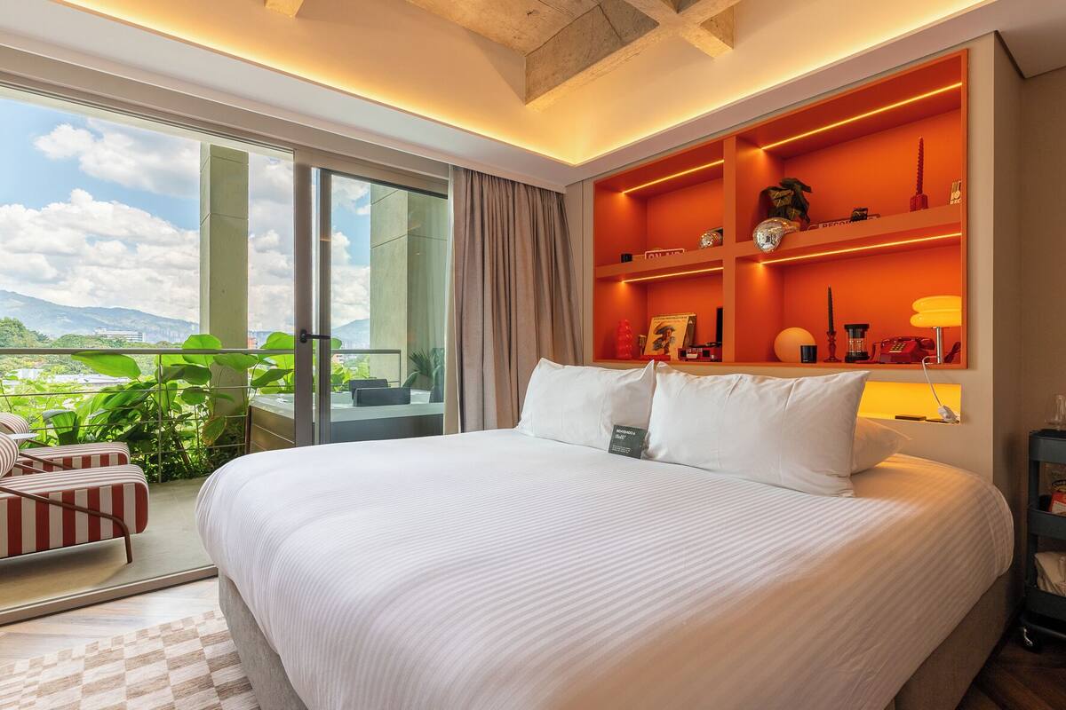 Ein Hotelzimmer mit einem großen Bett, einem Balkon mit Aussicht und einer leuchtend orangefarbenen Akzentwand.