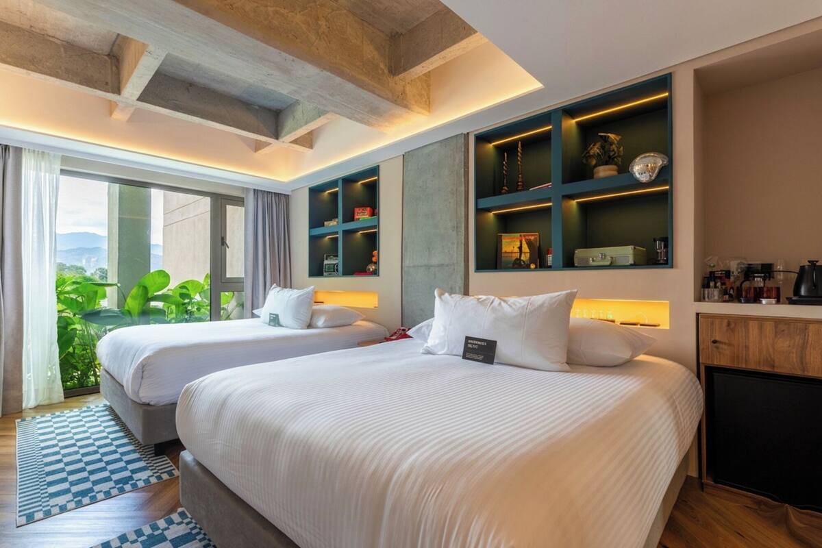 Ein Hotelzimmer mit zwei Betten, Blick ins Grüne, einer Minibar und einem Schreibtisch.