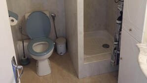 A small bathroom with a toilet, a shower stall, and a cabinet with shelves. - T2 apartment in residence 100 m from the beach. (Canet-en-Roussillon)