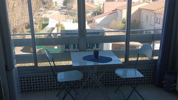 A balcony with a table and chairs, a potted plant, and a view of the surrounding neighborhood. - T2 apartment in residence 100 m from the beach. (Canet-en-Roussillon)