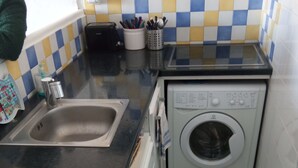 A compact kitchen with a sink, a washing machine, and a tiled backsplash. - T2 apartment in residence 100 m from the beach. (Canet-en-Roussillon)
