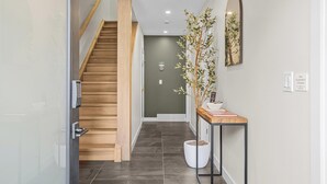 A modern hallway with a wooden staircase, a potted plant, and a small table with a mirror and a sign. - Sisters' Solstice - Stunning Mountain Views with Private Hot tub, Sauna & BBQ! (Canmore)