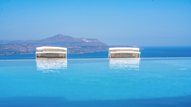 Ein Pool mit zwei Liegestühlen, mit Blick auf Berge und Meer.