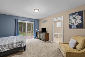 A bedroom with a bed, a dresser, a sofa, a painting, and a sliding glass door leading to a balcony. - Wooded Retreat w/ Hot Tub near Schweitzer (Sandpoint)