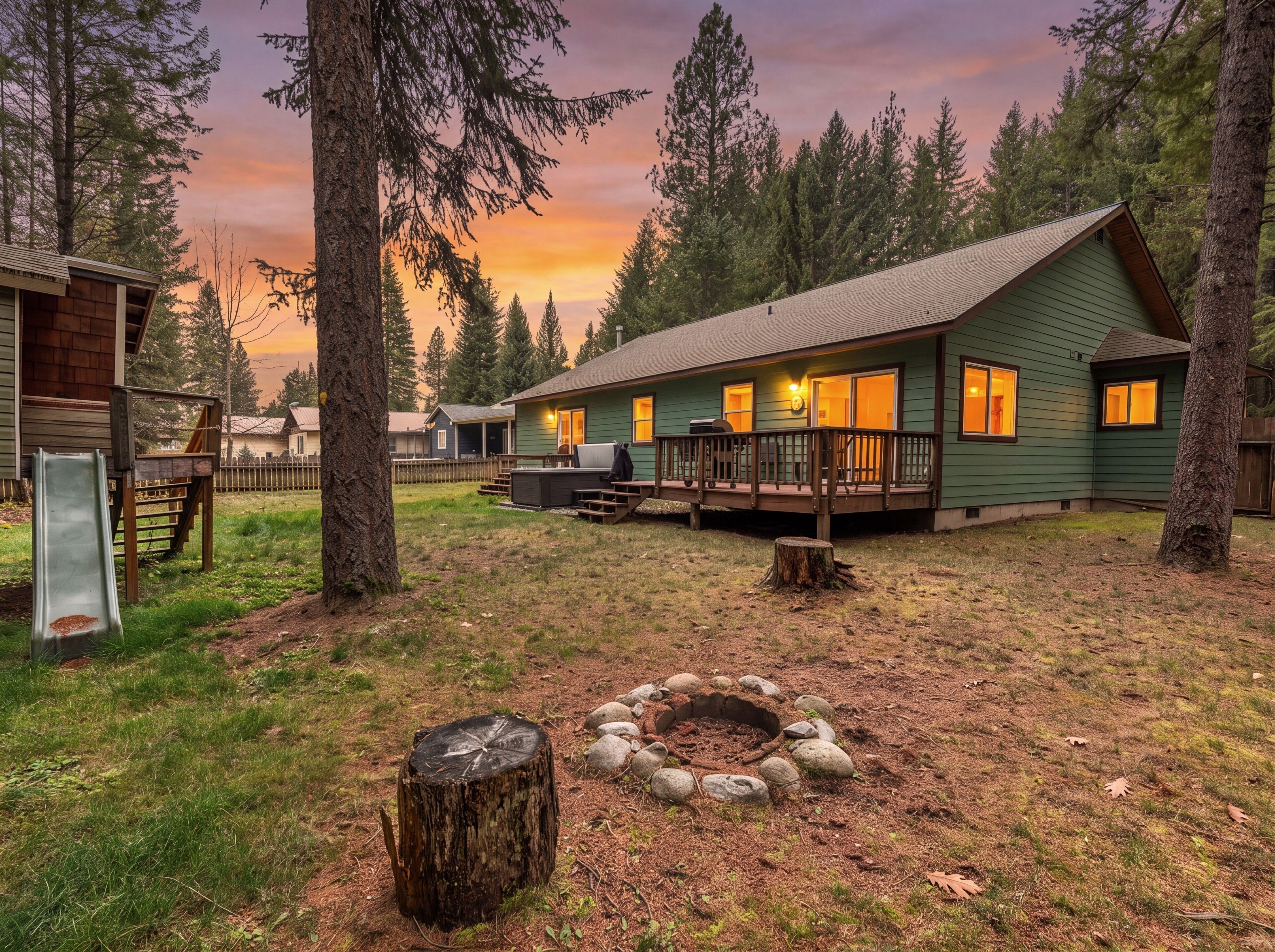 A cabin with a deck, a fire pit, and a slide in a forested area.