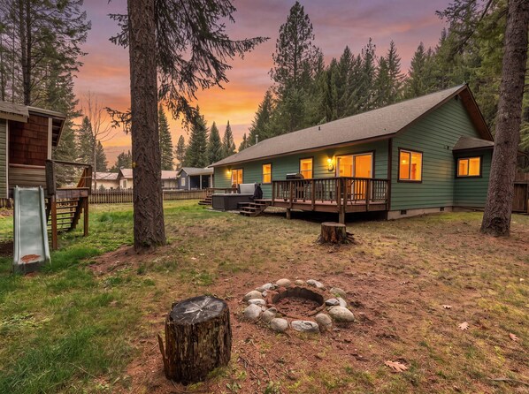 A cabin with a deck, a fire pit, and a slide in a forested area. - Wooded Retreat w/ Hot Tub near Schweitzer (Sandpoint)