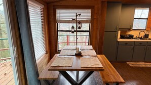A wooden dining table with four placemats, a hanging lantern, and a view of a kitchen and deck through a window. - Dogwood Legend 3 Mins From DTWN Jasper (Jasper)