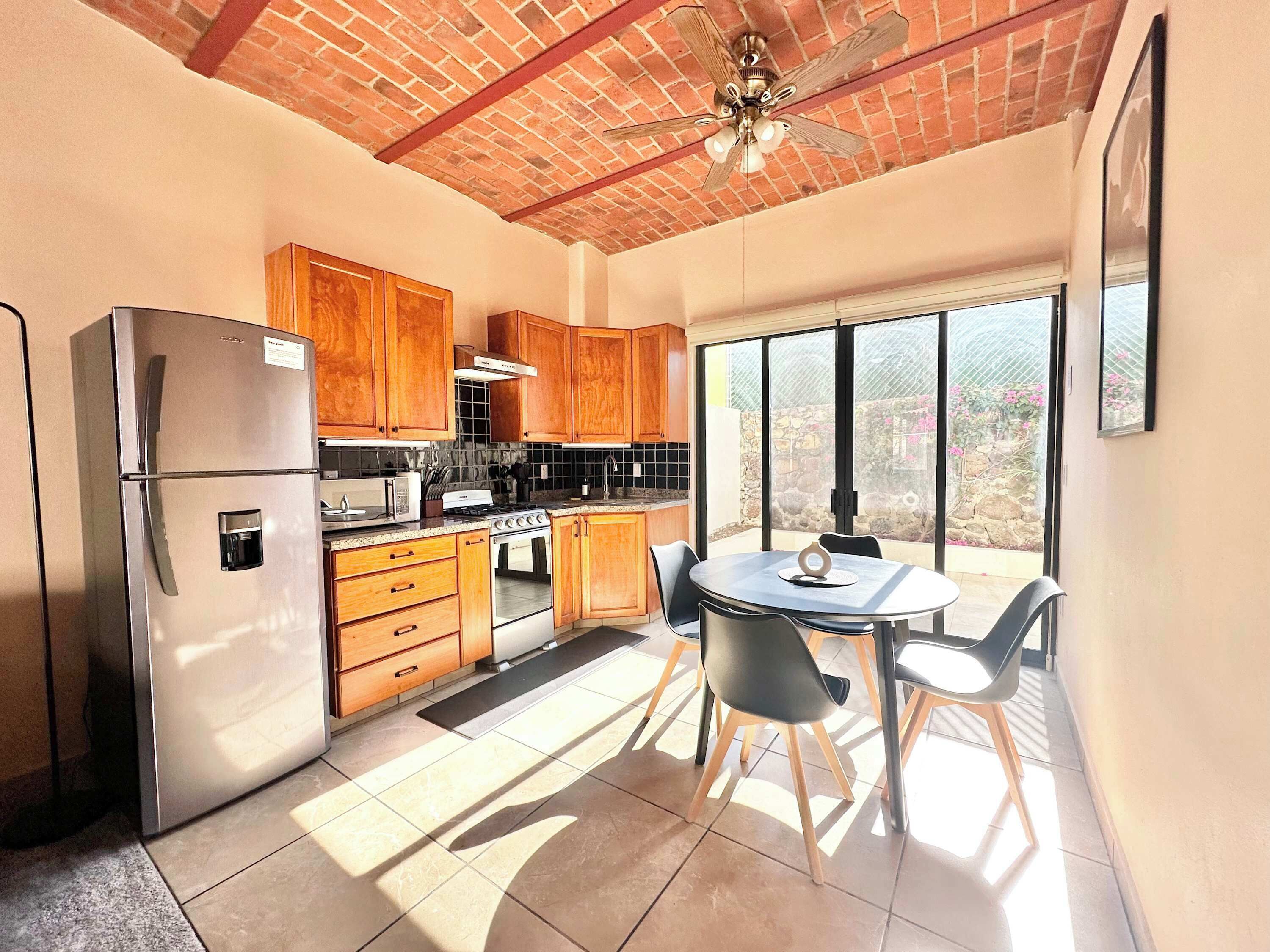 Una cocina con refrigerador, estufa, armarios de madera y un comedor con sillas y mesa.