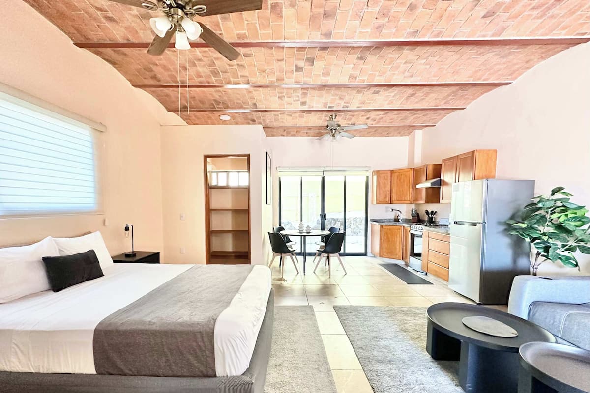 Une chambre d’hôtel moderne équipée d’un lit, d’un coin repas, d’une kitchenette et d’un ventilateur de plafond.