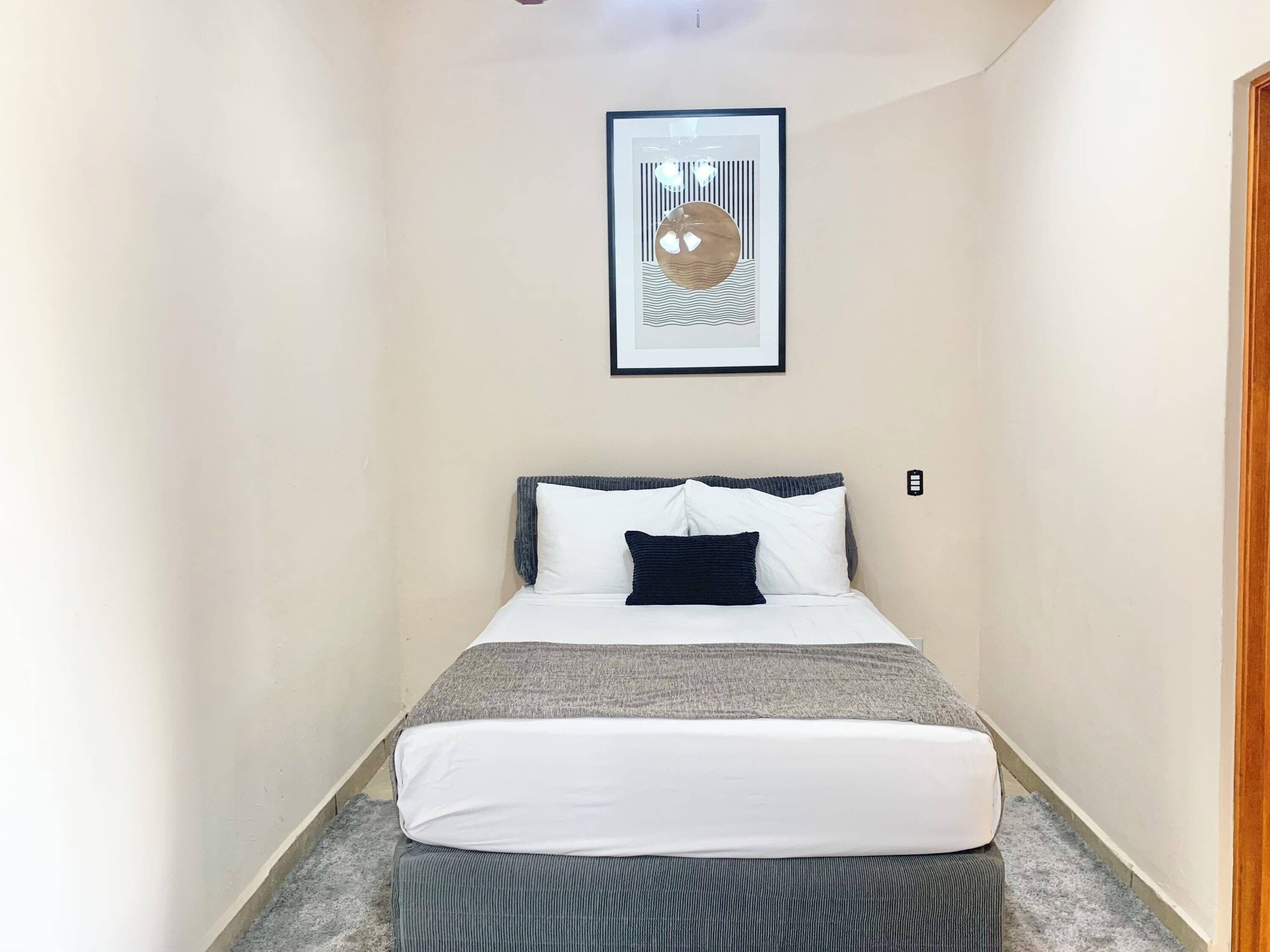 Een smalle hotelkamer met een bed, een inlijsting foto aan de muur, en een vloerkleed.