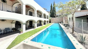 A pool with a clear blue water, surrounded by a white building with multiple balconies and a brick wall in the background. - Lirio, Ajijic (Ajijic)