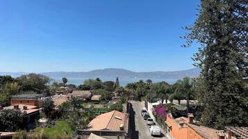 Una calle con edificios, automóviles estacionados y una vista despejada del mar y las montañas al fondo.