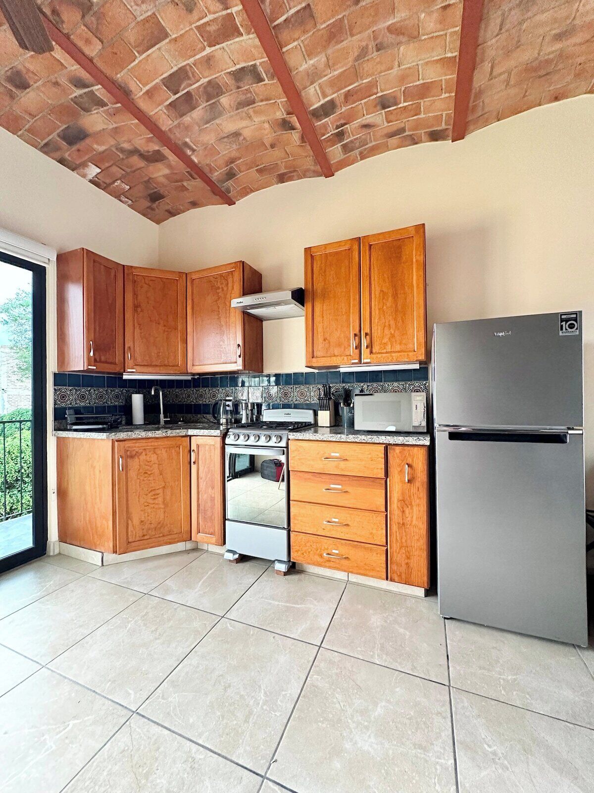 A kitchen with wooden cabinets, a stainless steel refrigerator, a stove, and a microwave.
