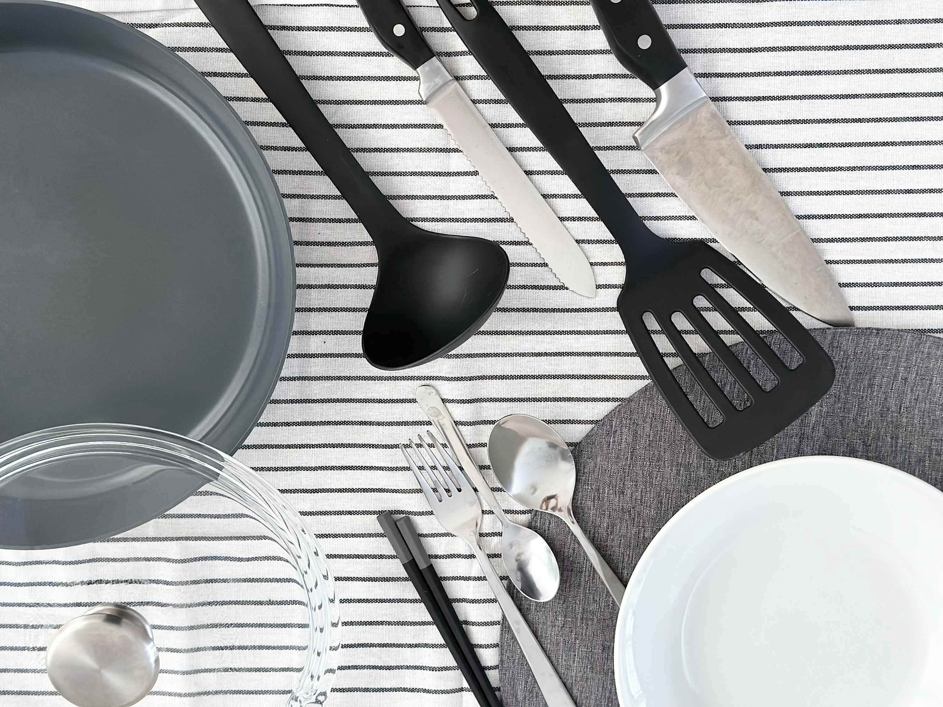 Un piano di lavoro in cucina con una pentola grande, spatole nere, un coltello, un cucchiaio e una forchetta, e un piatto.