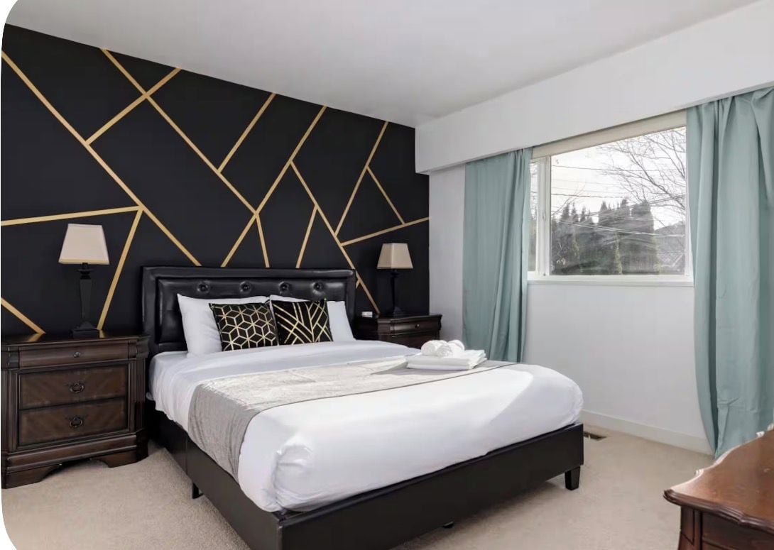 Ein Hotelzimmer mit einem Bett, Nachttischen, einem Fenster mit Vorhängen und einem geometrischen Wanddesign.