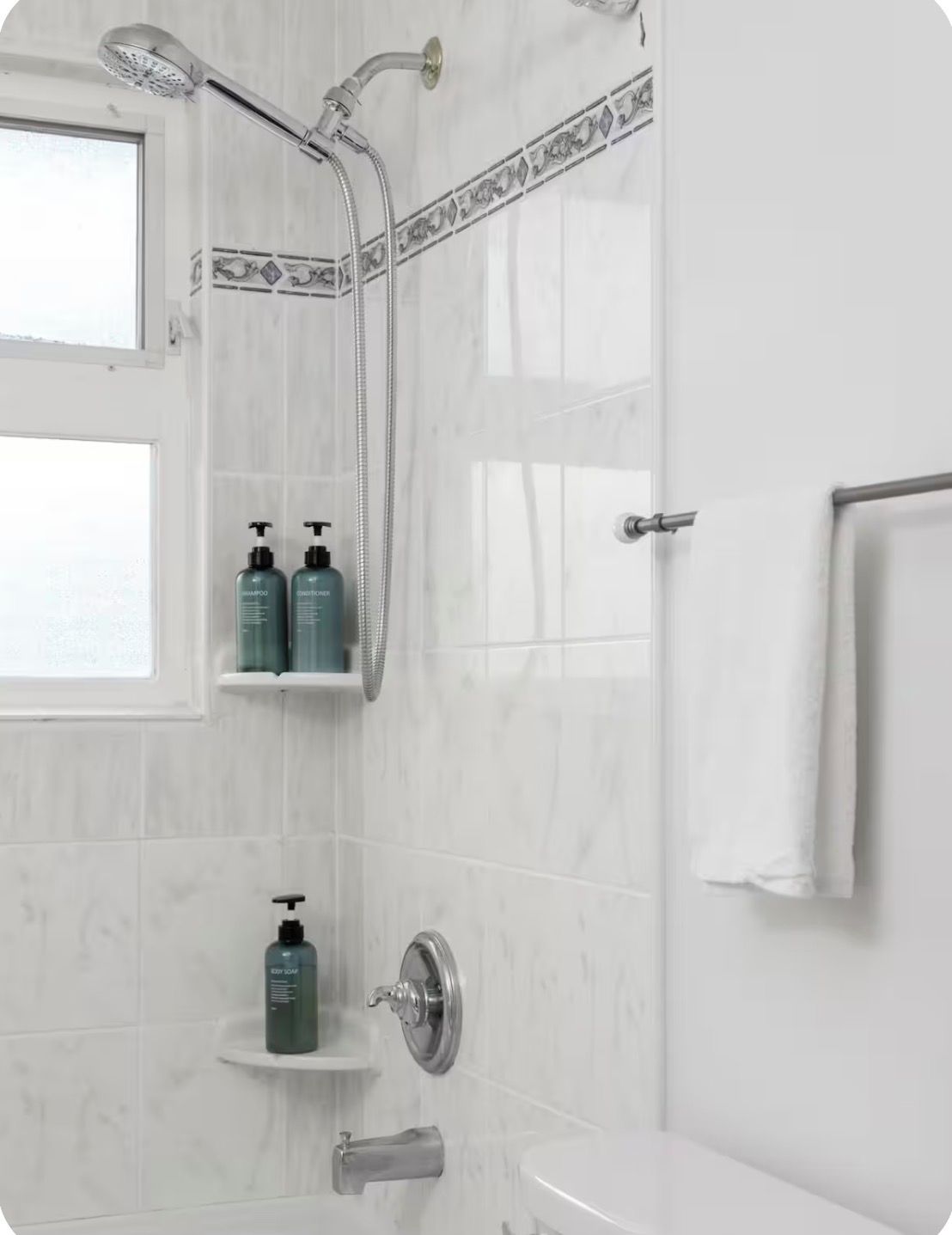Un baño con ducha, inodoro y ventana. Hay dos repisas con artículos de aseo.