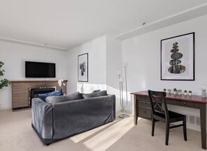 A modern living room with a sofa, a fireplace, a flat-screen TV, and a desk with a chair. - Lovely 2Br Home In Foster Ave. (Coquitlam)