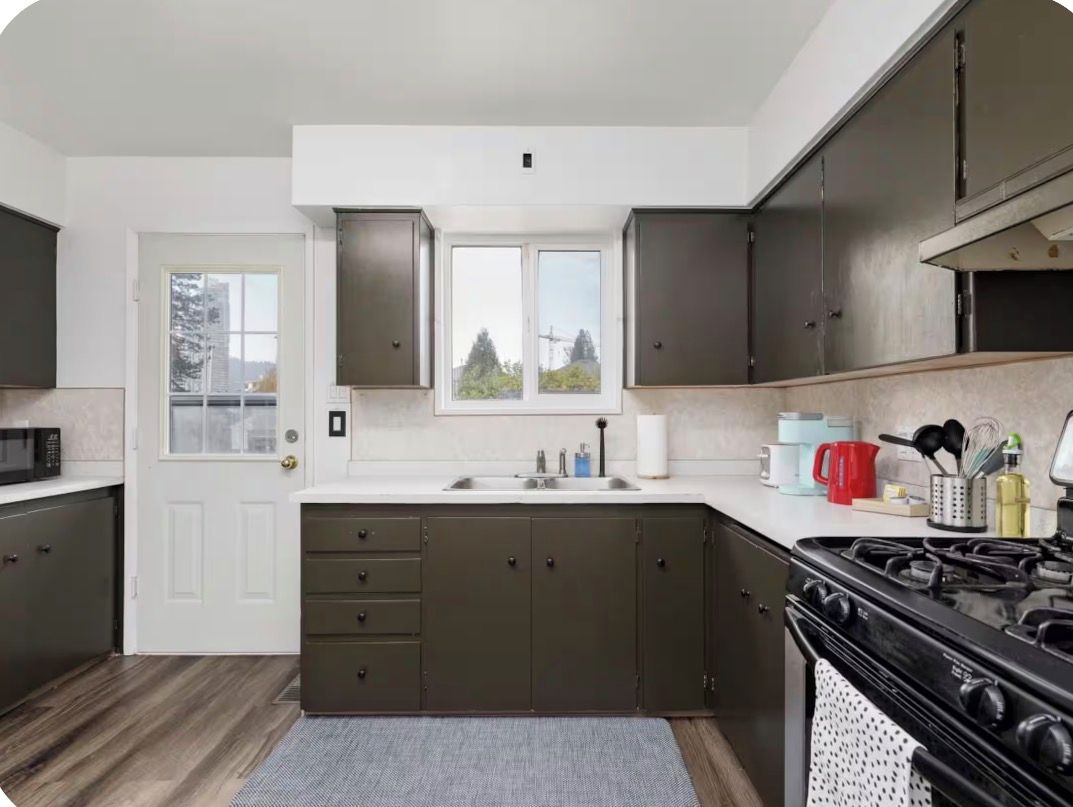 Une cuisine avec des meubles de rangement de couleur sombre, une cuisinière et une fenêtre donnant sur des arbres.
