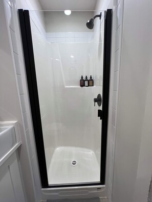 Eine Dusche mit Glastür, weißen Fliesen und Ablage für Toilettenartikel.