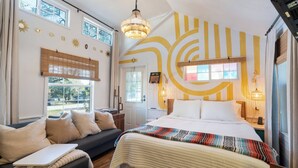 Un dormitorio con una cama grande, un sofá y un escritorio. Hay ventanas, una puerta y una pared con detalles decorativos.