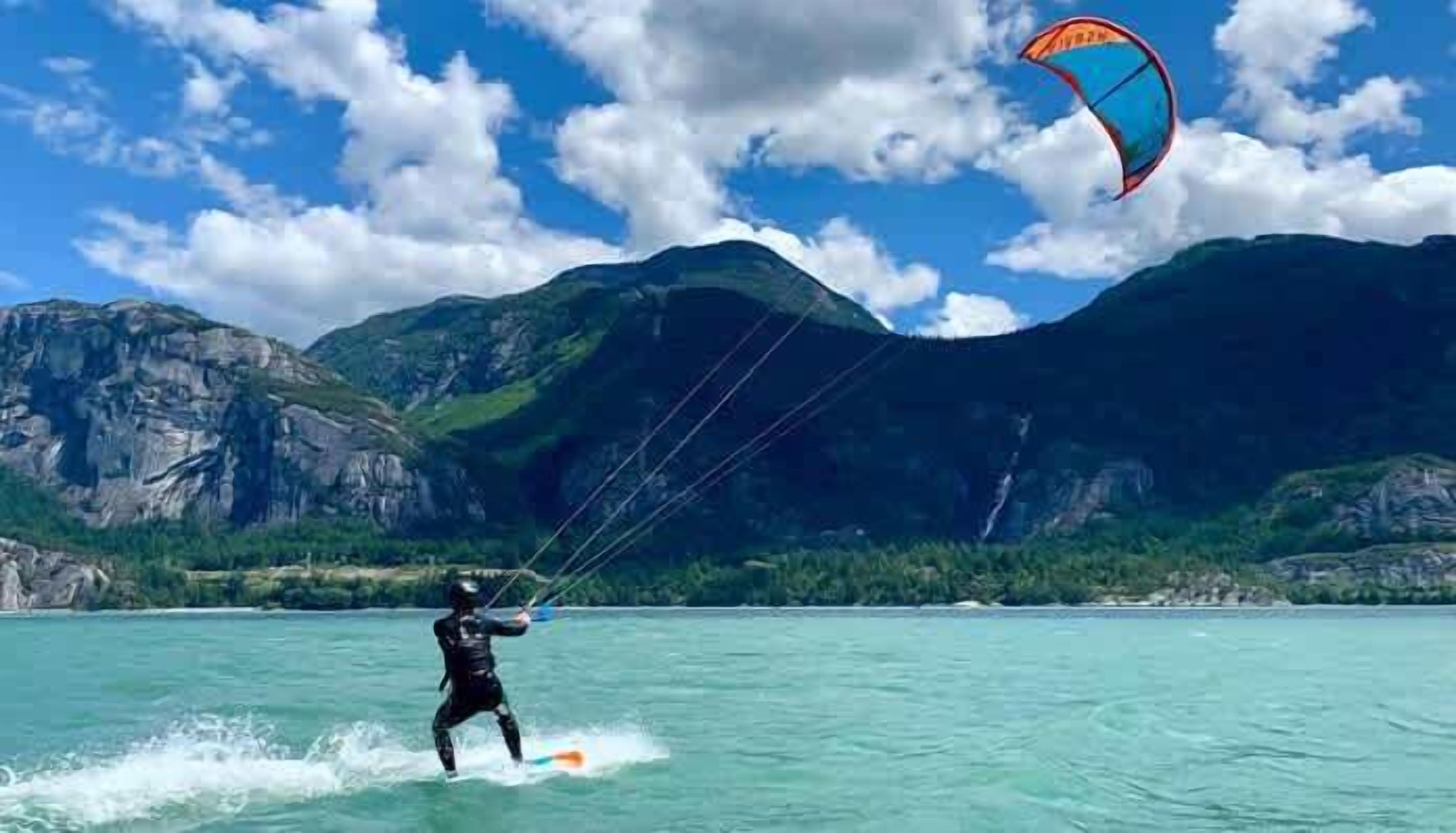 A person windsurfing on a body of water with mountains in the background.