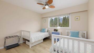 Un dormitorio con dos camas, ventilador de techo, ventana con vistas a árboles y radiador.