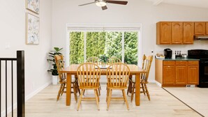 Ein Essbereich mit Tisch und Stühlen, einem Deckenventilator, einem Fenster mit Blick auf Bäume und Küchenschränken aus Holz.