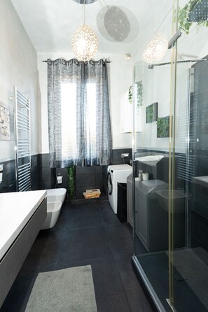 A modern bathroom with a glass shower enclosure, a built-in washing machine, and a large window with curtains. - CupolHome - Meraviglia a San Pietro (Roma)