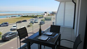 Ein Balkon mit Tisch für zwei Personen, mit Blick auf einen Parkplatz und einen Strand.