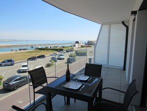 A balcony with a table set for two, overlooking a parking lot and a beach. - Comfortable apartment with exceptional view of port, beach and sea (Barneville-Carteret)